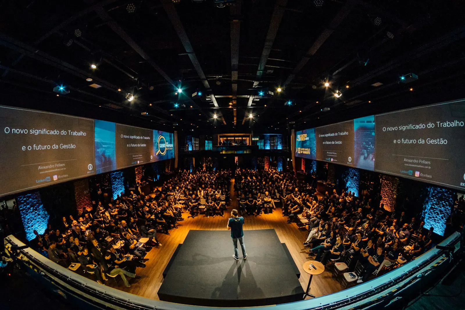 Speaker on stage in front of LED screens and a seated audience